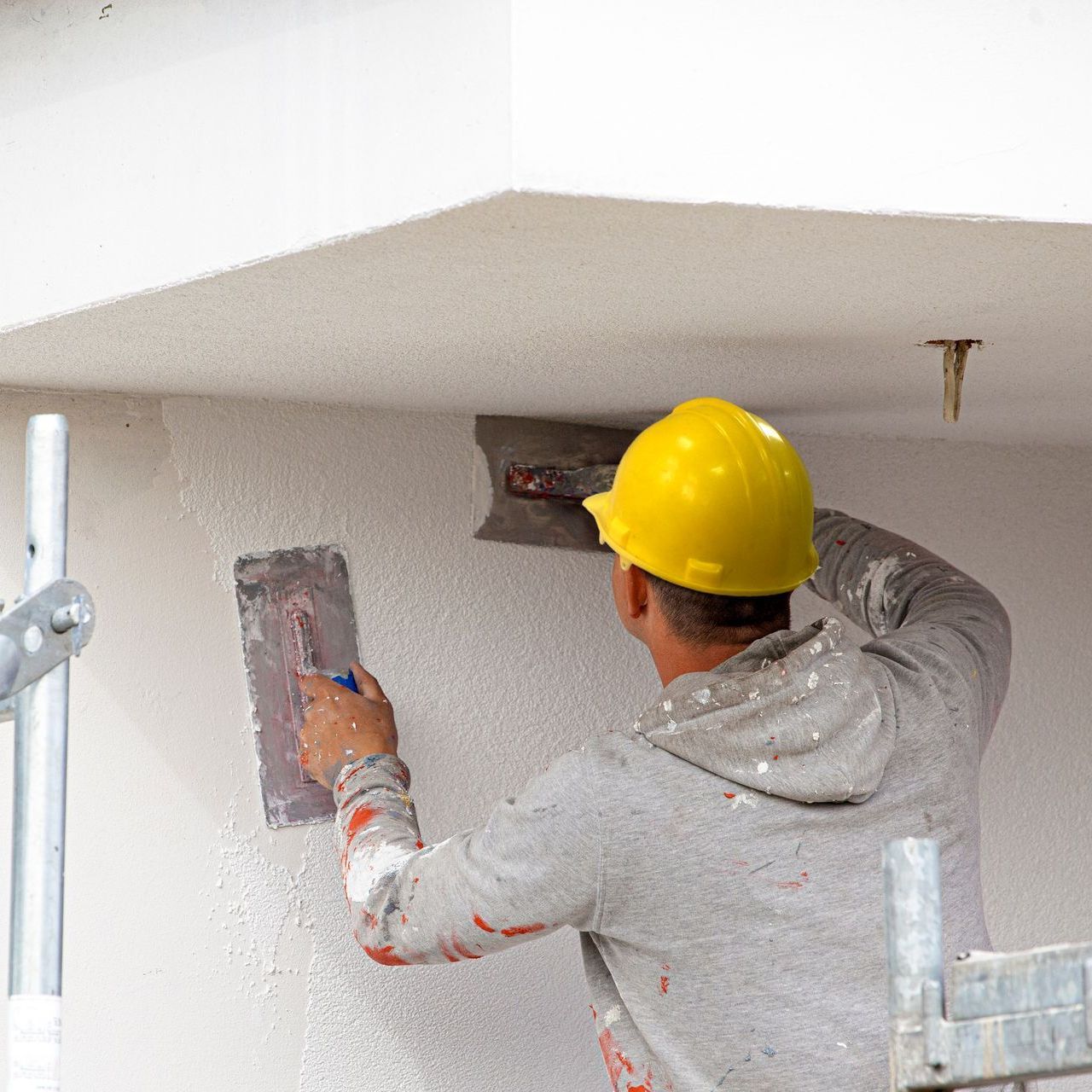a man wearing a yellow hard hat is plastering a wall .