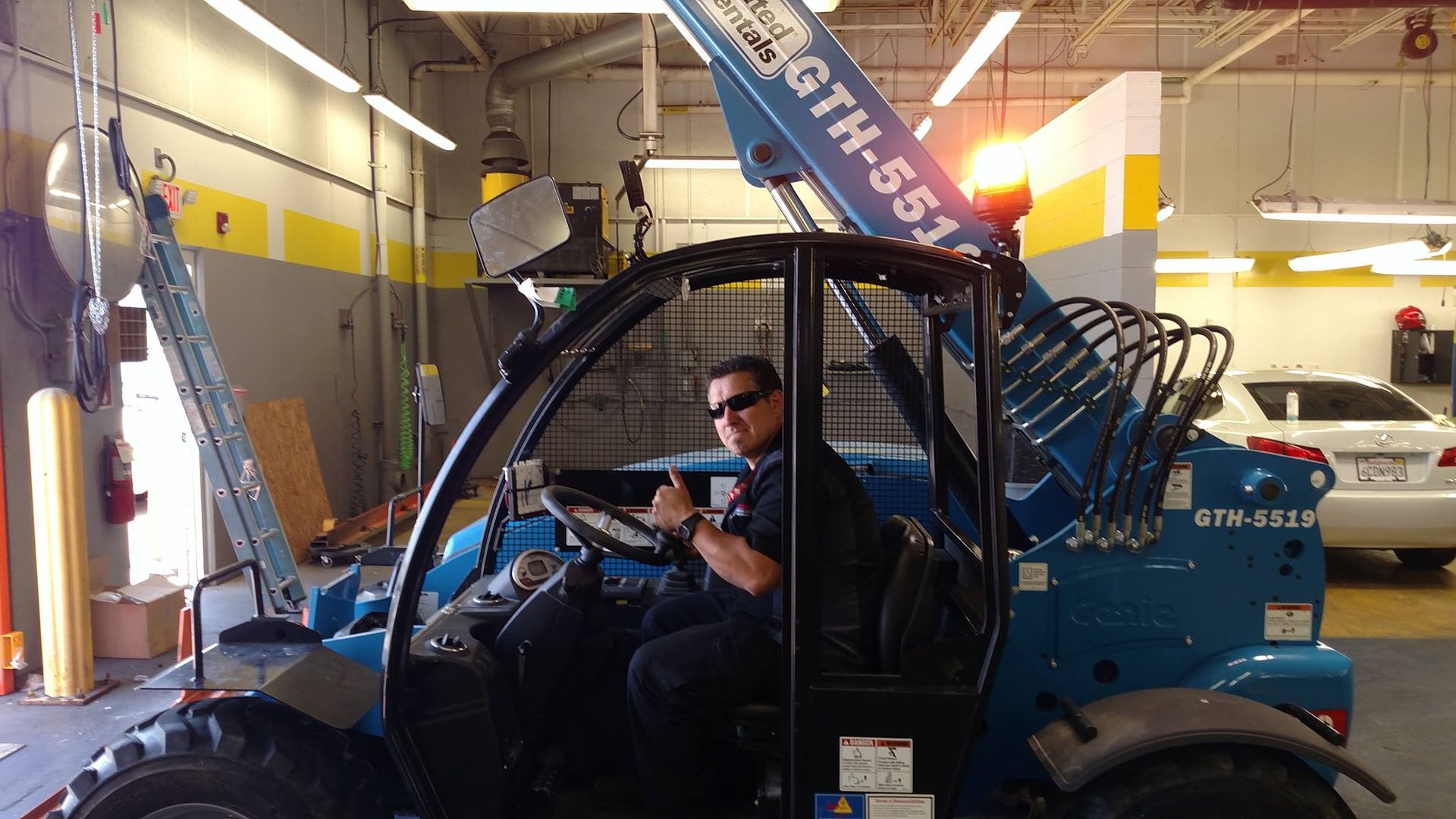 Person in a blue telehandler gives a thumbs-up in a garage.