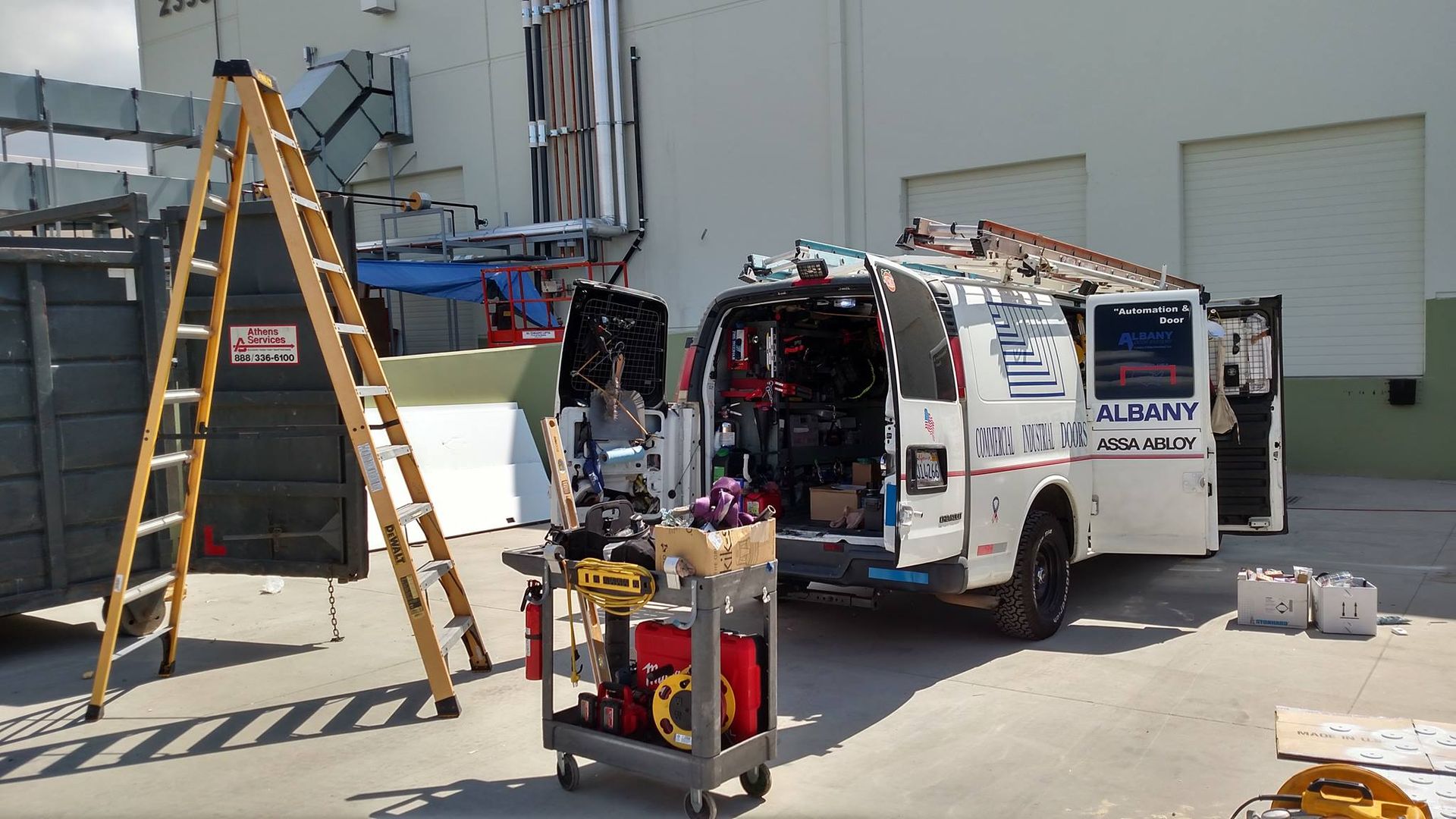 A white van is parked in front of a building with tools in the back.
