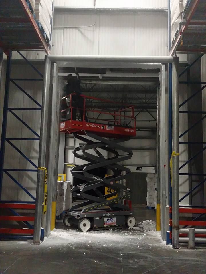 A red scissor lift in an open warehouse bay with a person on the lift.