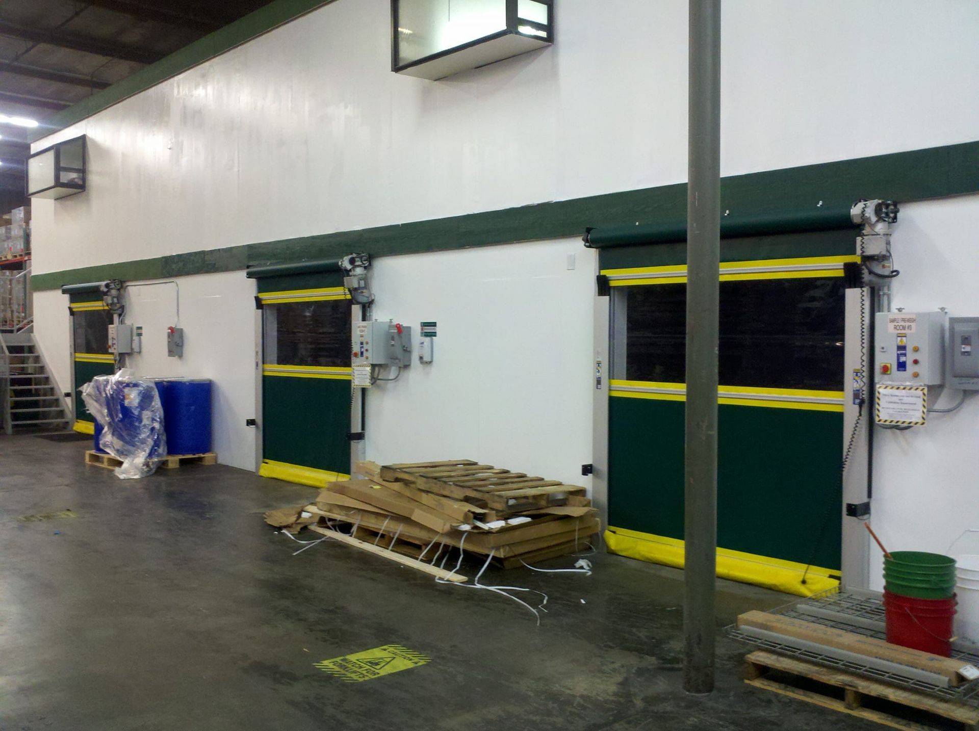 A warehouse with green and yellow doors and pallets on the floor