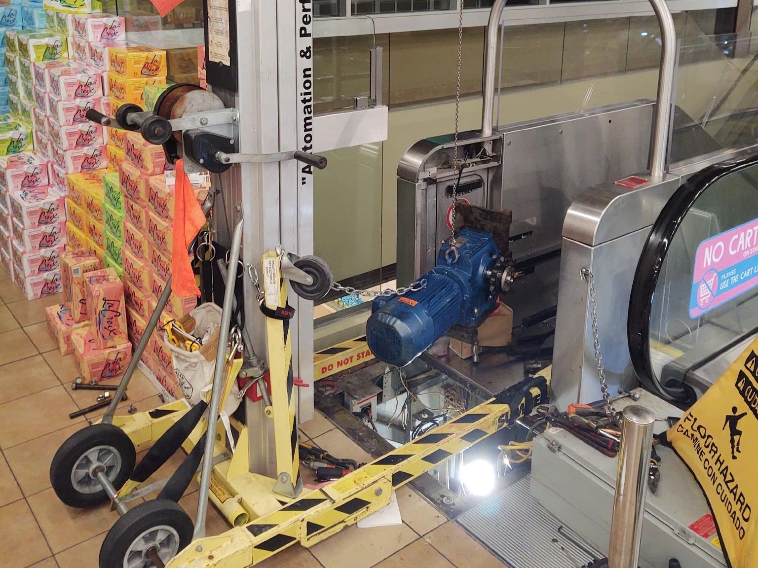 A deactivated escalator in a store; repair work in progress with a lift, barriers, and caution tape.
