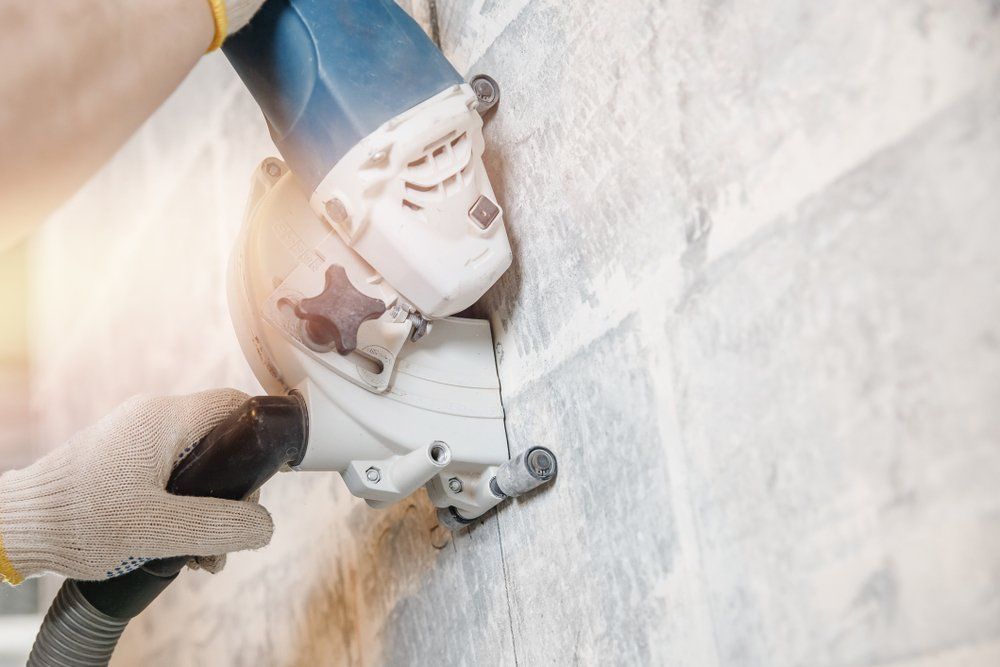 A person using a power saw to cut tile on a wall, with a vacuum hose attached, for construction work.