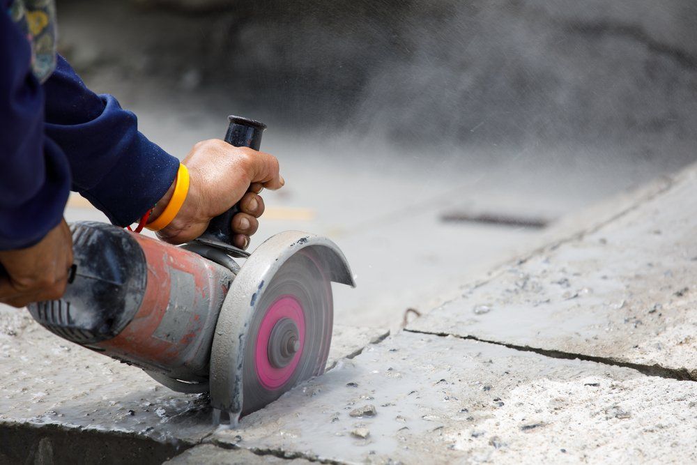 Person using an angle grinder to cut concrete; dust is visible.