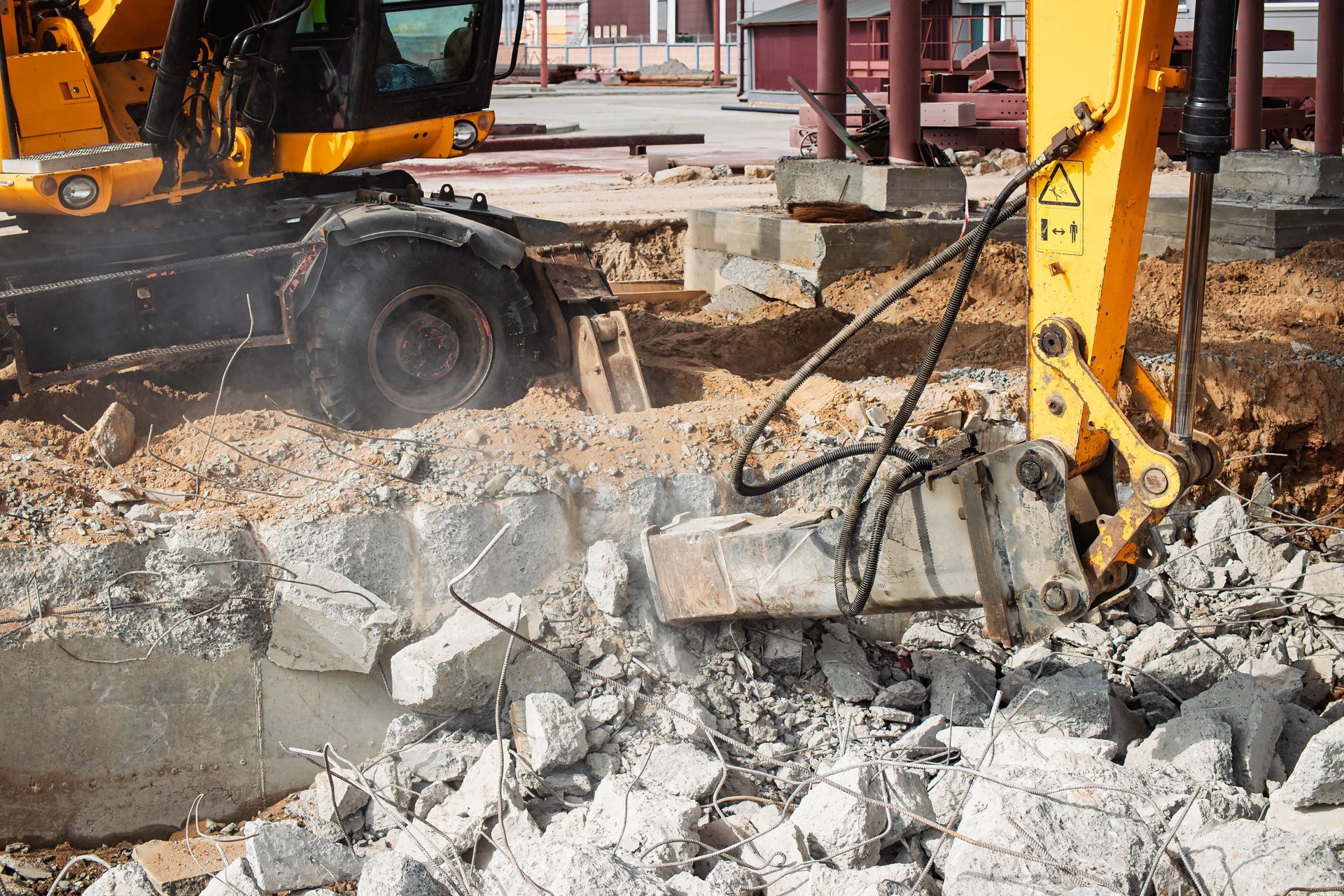 Yellow excavator demolishing concrete structure on a construction site.