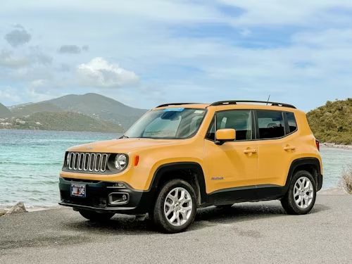 A yellow jeep renegade is parked on the side of the road near the ocean.