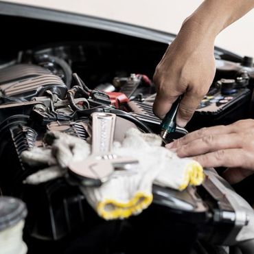 A person is working on the engine of a car with a screwdriver.