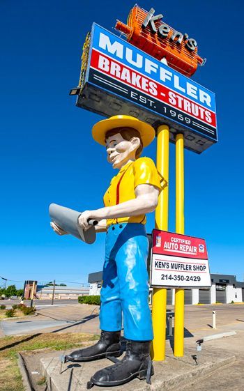 A statue of a man is standing in front of a sign for muffler brakes and struts.