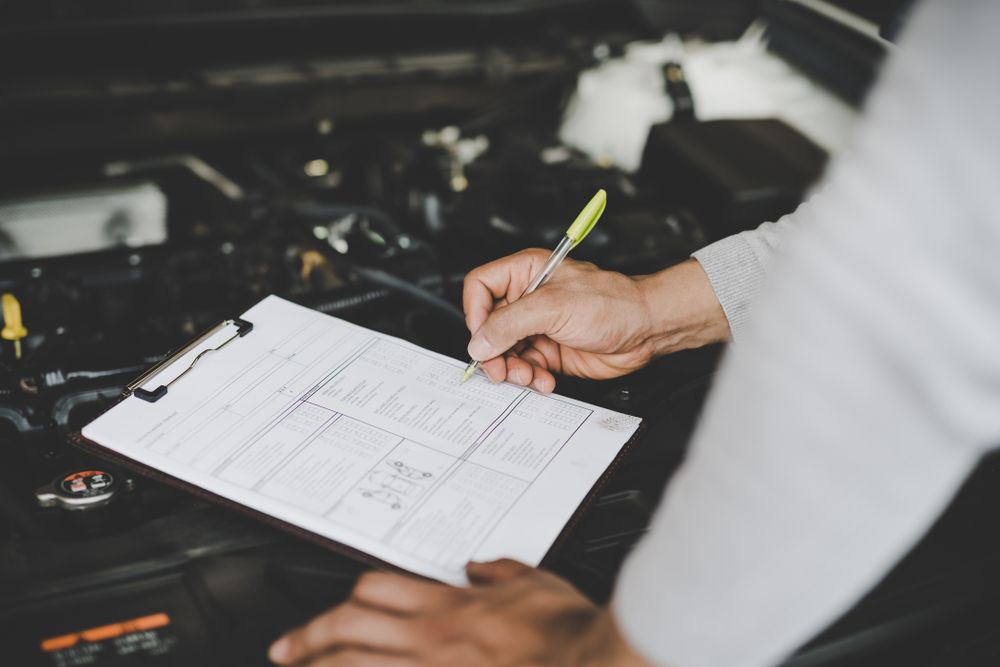 A Technician Writes on a Clipboard While Inspecting an Open Car Engine — Roberts Automotive & Industrial in Brighton, TAS