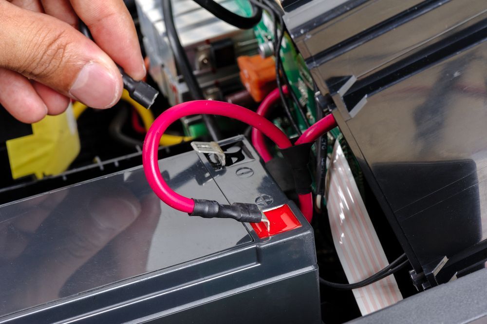 A Hand Holds a Detached Wire Connector Near a Red-tipped Terminal of a Lead-acid Battery — Roberts Automotive & Industrial in Brighton, TAS
