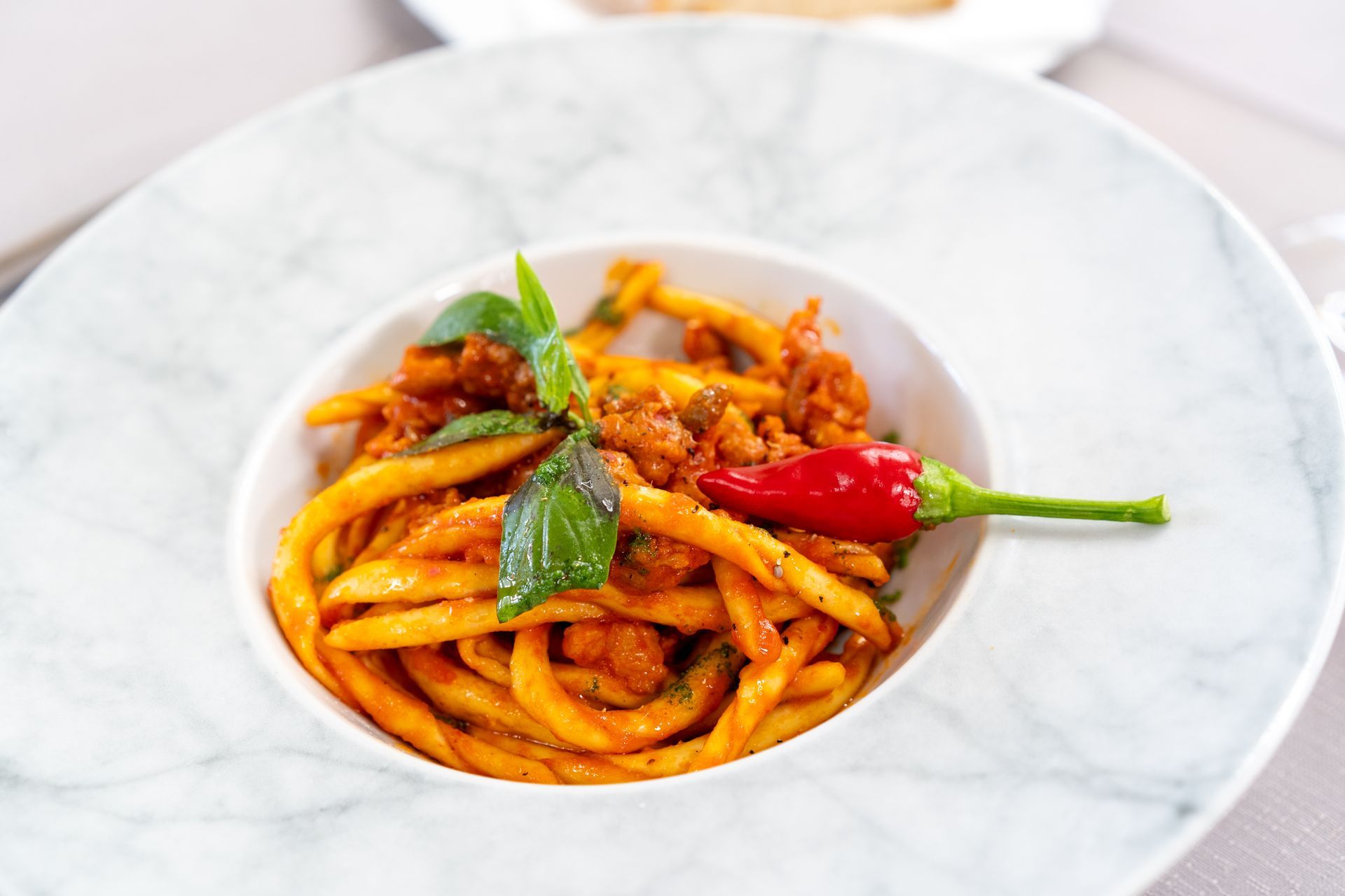 Piatto di pasta in una ciotola di marmo bianco, guarnito con basilico e un peperoncino rosso.