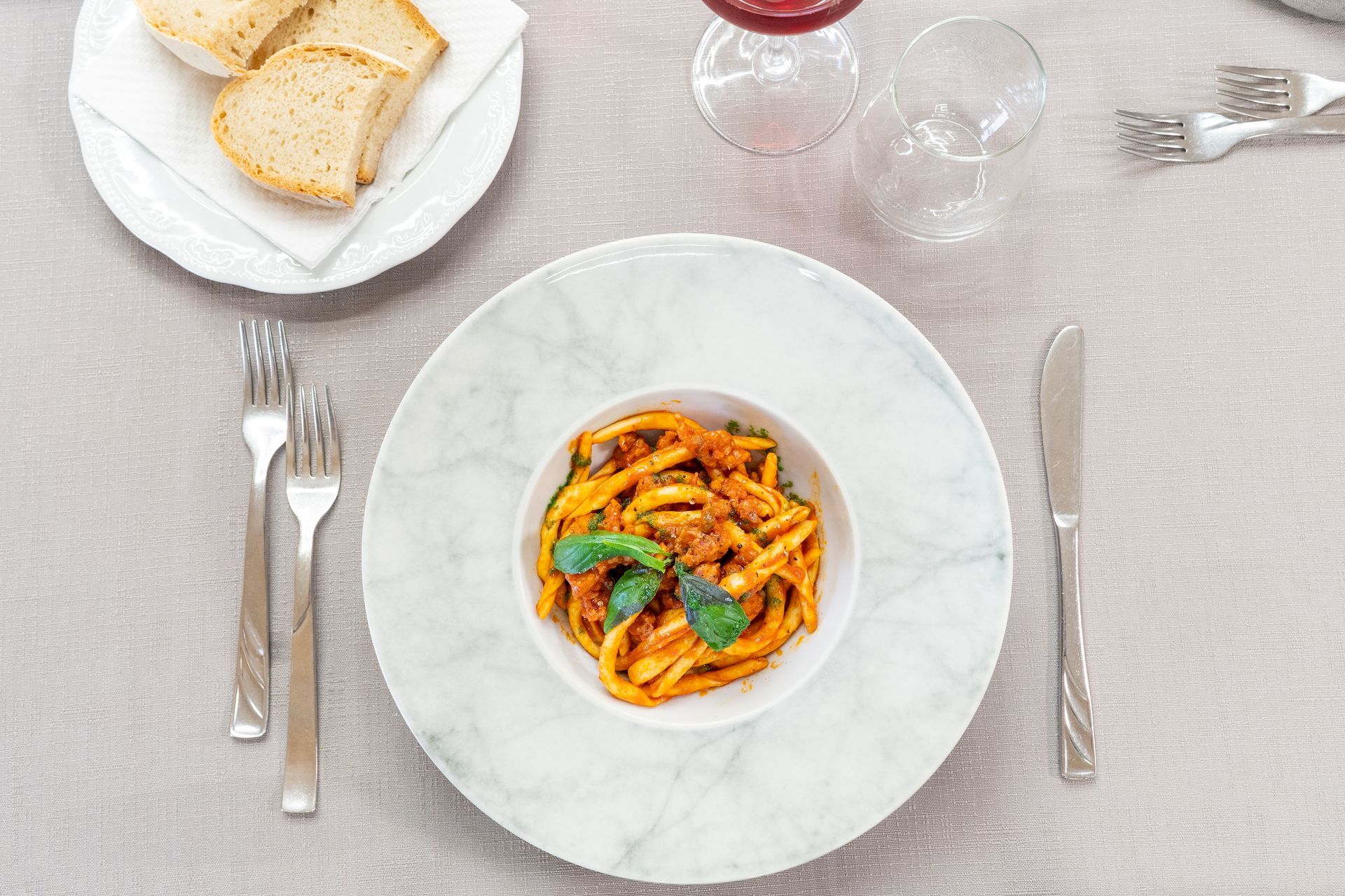 Piatto di pasta con pane, posate e bicchieri da vino su una tavola apparecchiata per cenare.