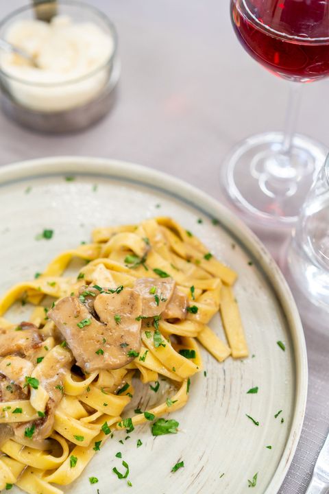 Fettuccine con salsa cremosa ed erbe aromatiche su un piatto, accompagnate da un bicchiere di vino rosso e parmigiano.
