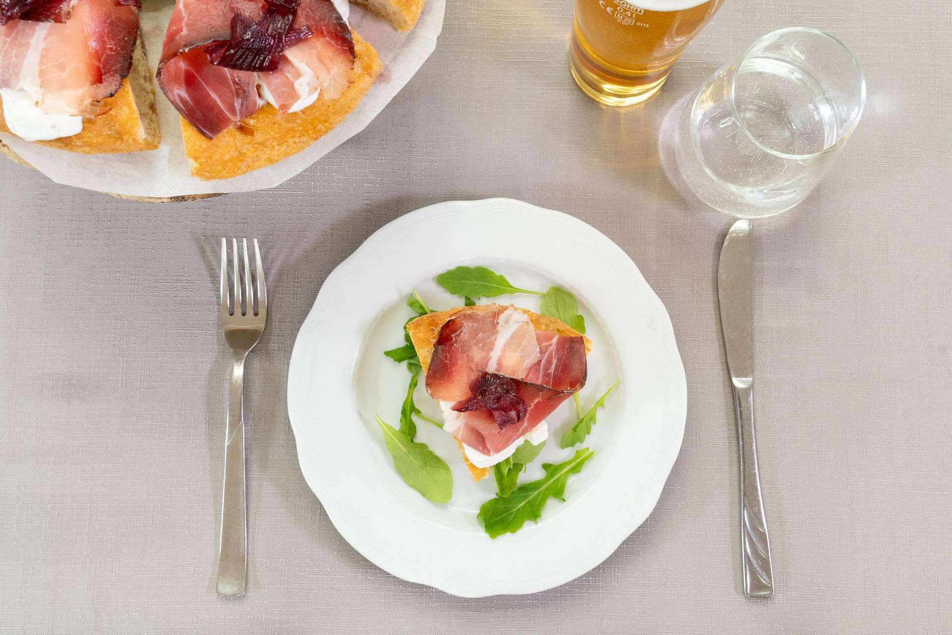Piatto con cibo (pizza), forchetta, coltello, bicchiere di birra, bicchiere d'acqua su un tavolo.