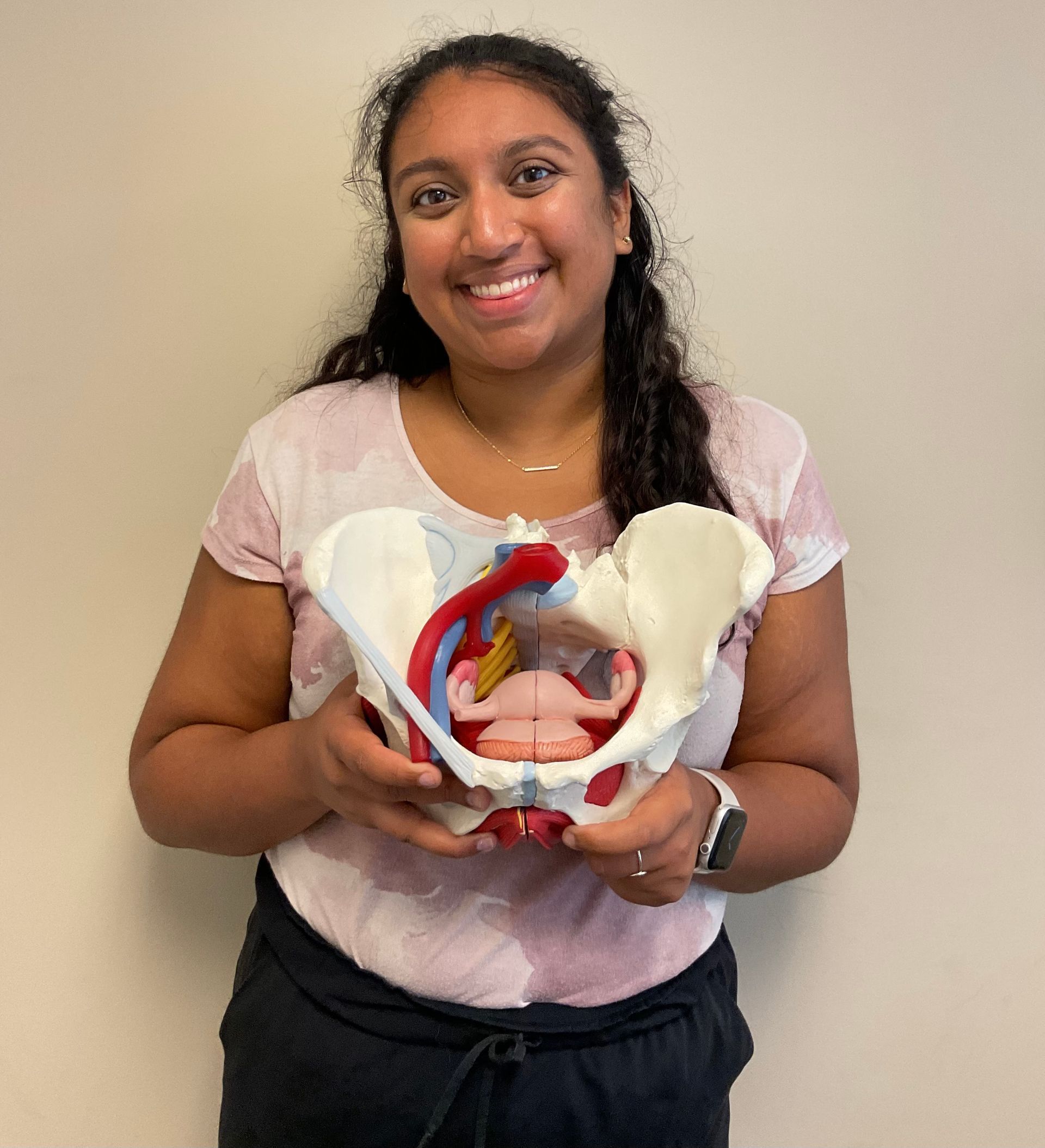A woman is holding a model of a woman 's pelvis and smiling.