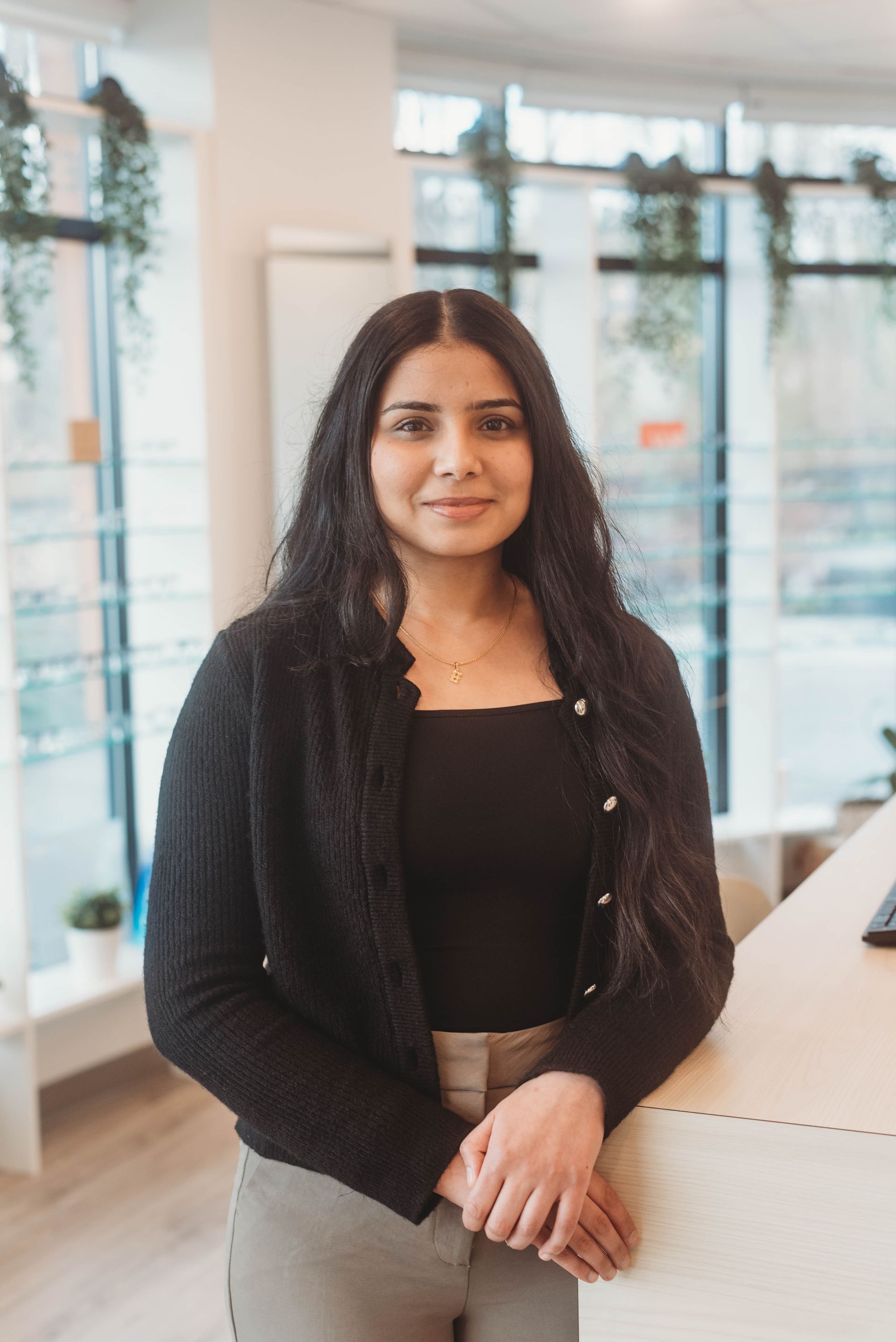 Woman in black top and sweater, standing indoors, smiling.