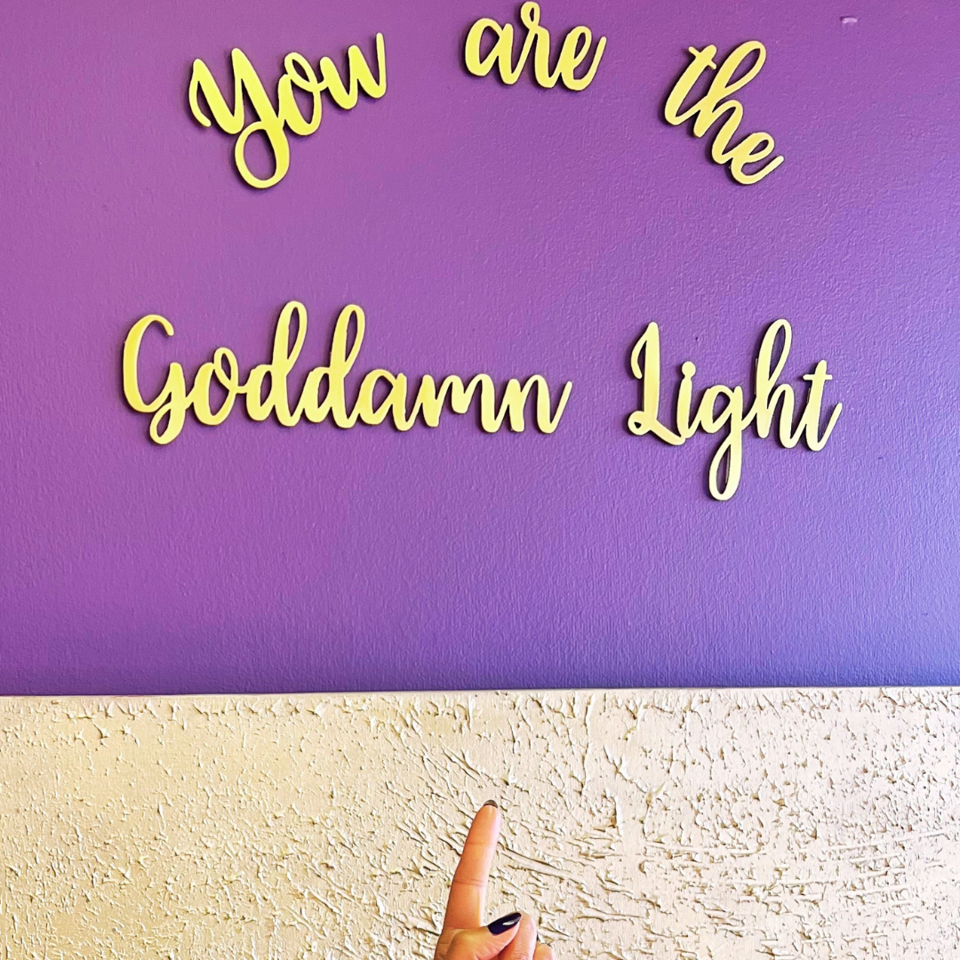 A metallic gold sign on a purple background with Dena Gould's motto