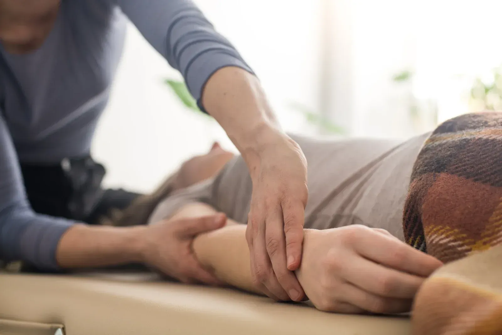 A person in a blue top gives a gentle massage to the arm of someone lying on a treatment table.