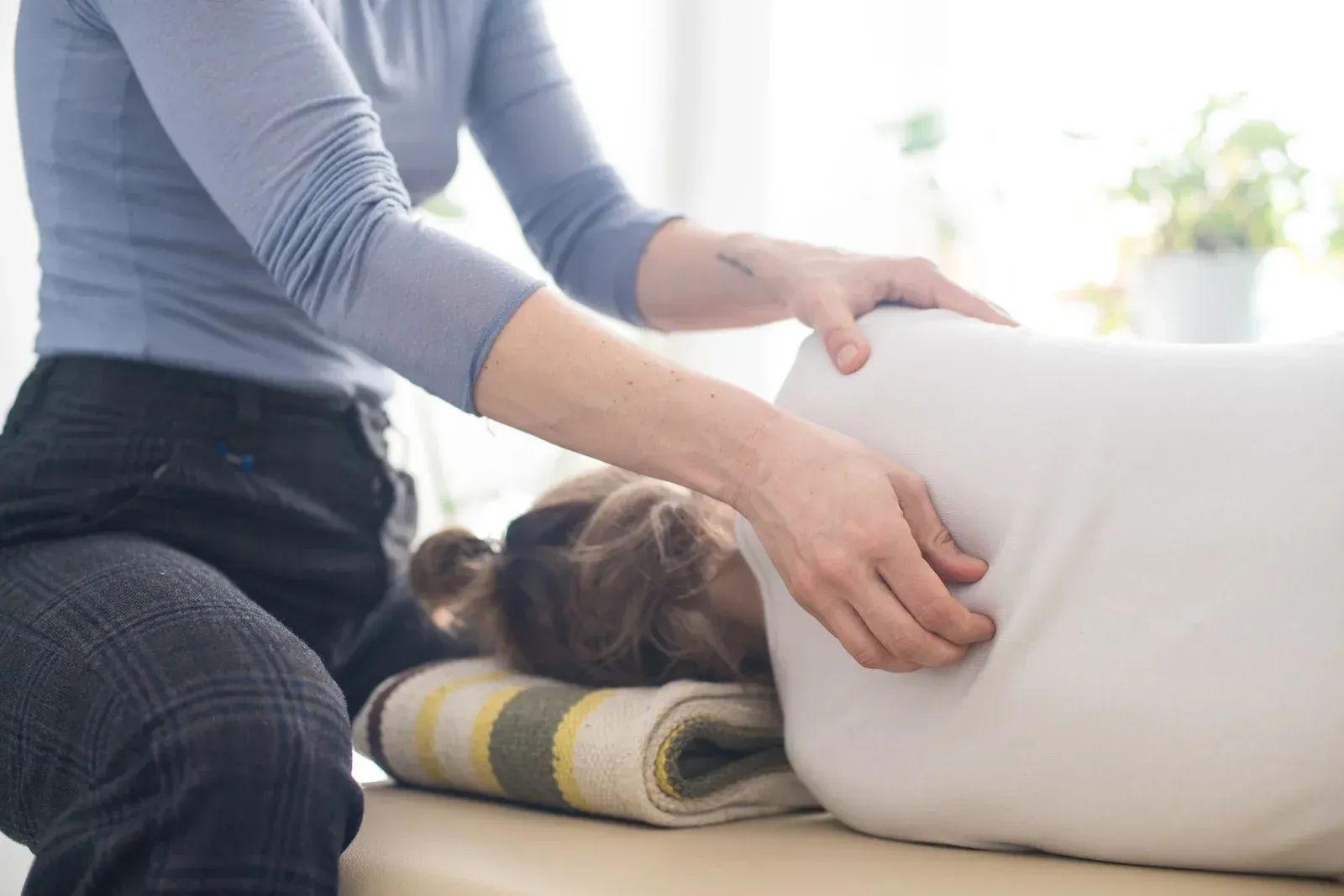 A person in a blue long-sleeved shirt performs massage therapy on the back of someone lying on a table.