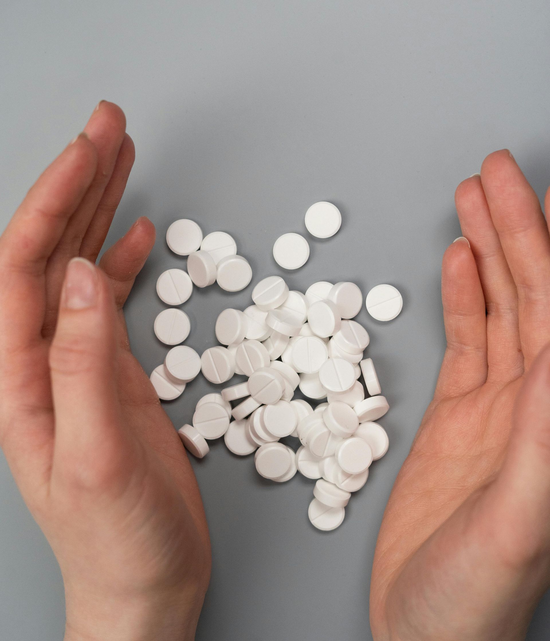 a person is holding a pile of white pills in their hands