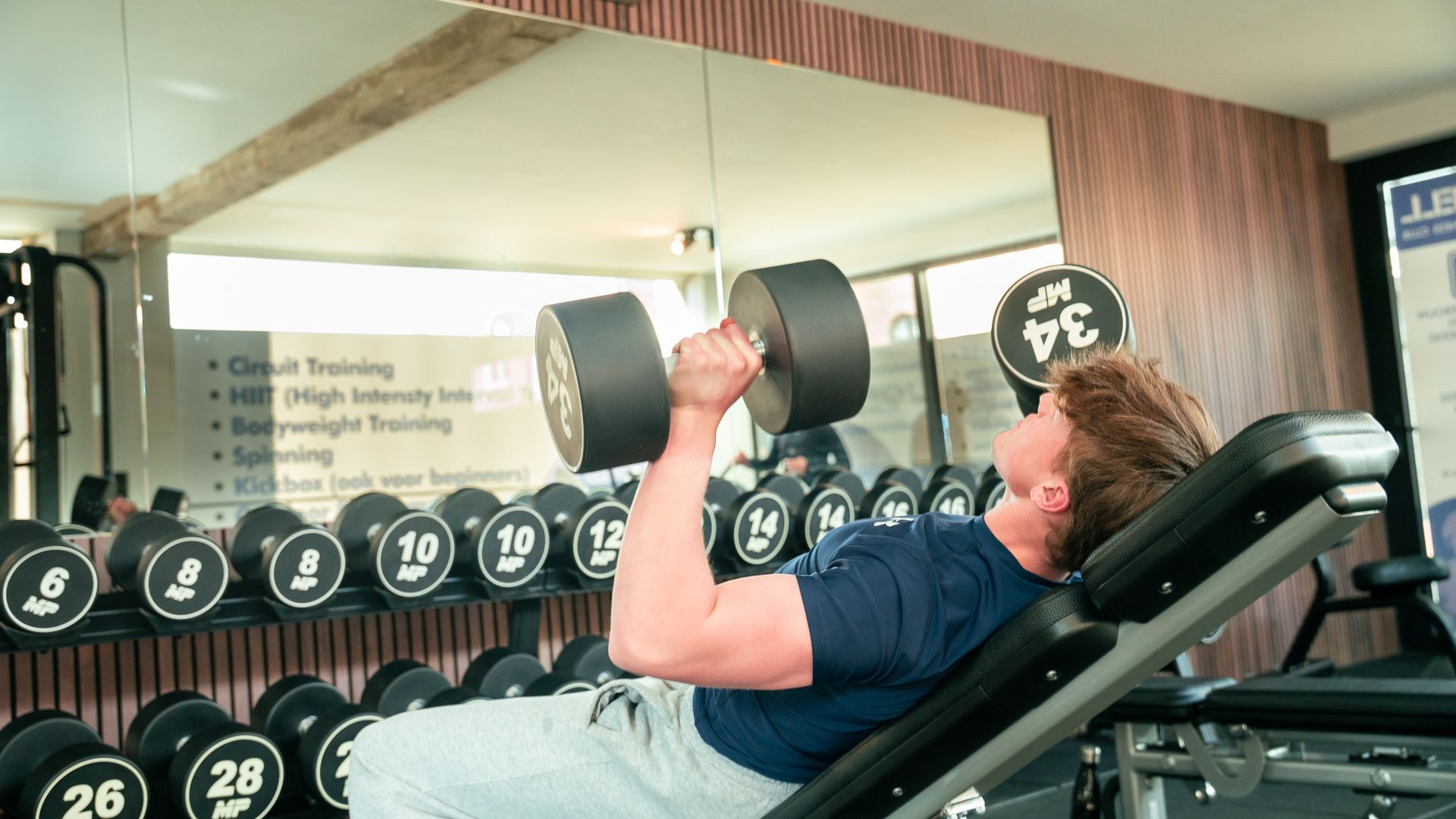 Een man tilt een halter op een bankje in een sportschool.