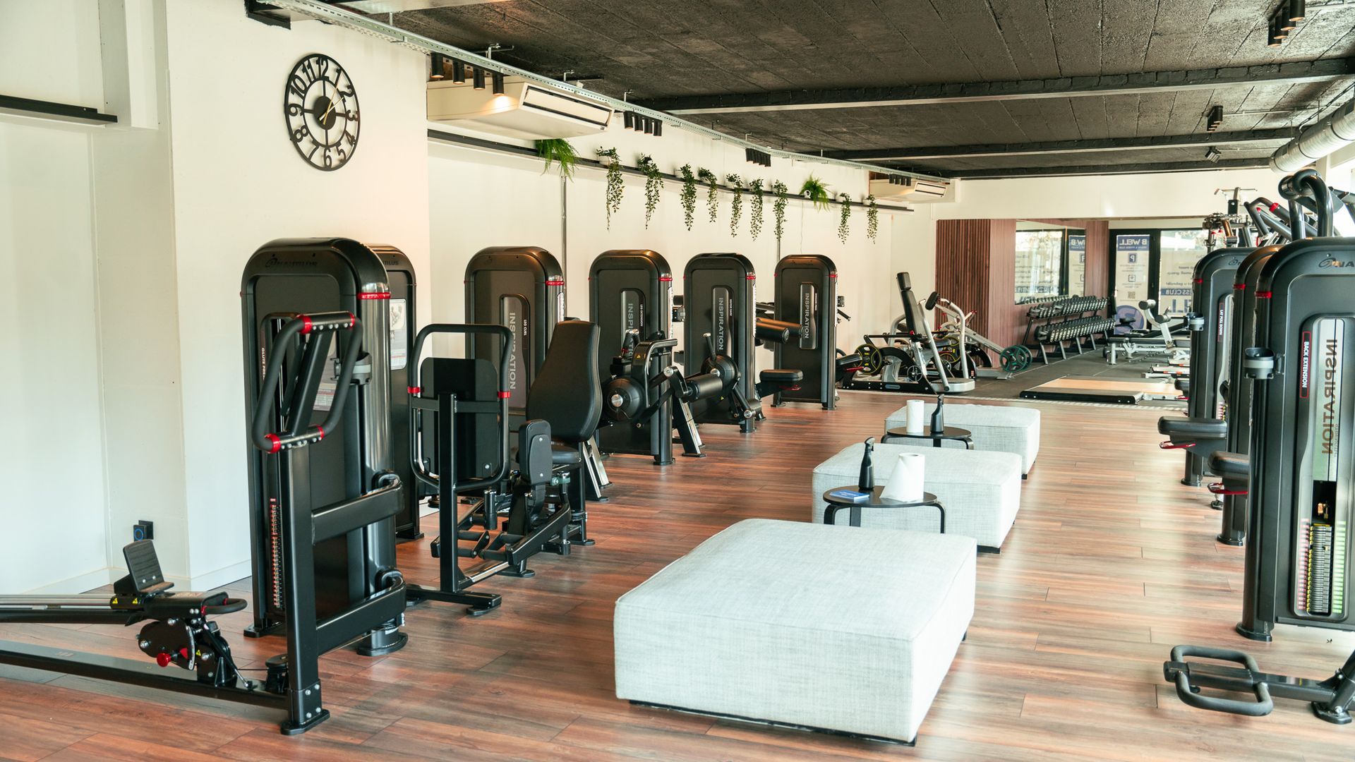 Een grote sportschool vol met fitnessapparatuur en banken.