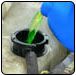 Pouring green coolant into a vehicle's radiator from a blue container. | Quality Car & Truck Repair