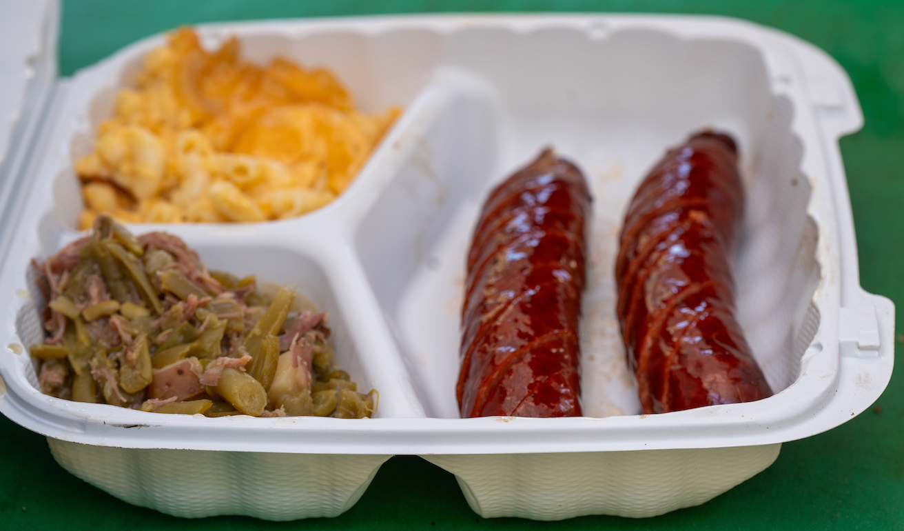 A plastic container filled with macaroni and cheese , green beans , and sausage.