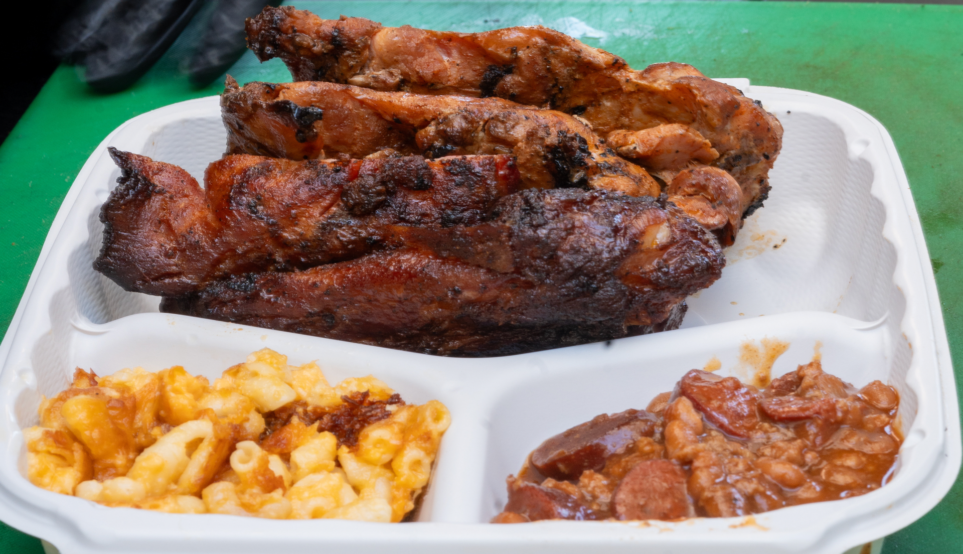 A plastic container filled with meat , macaroni and cheese , and beans.