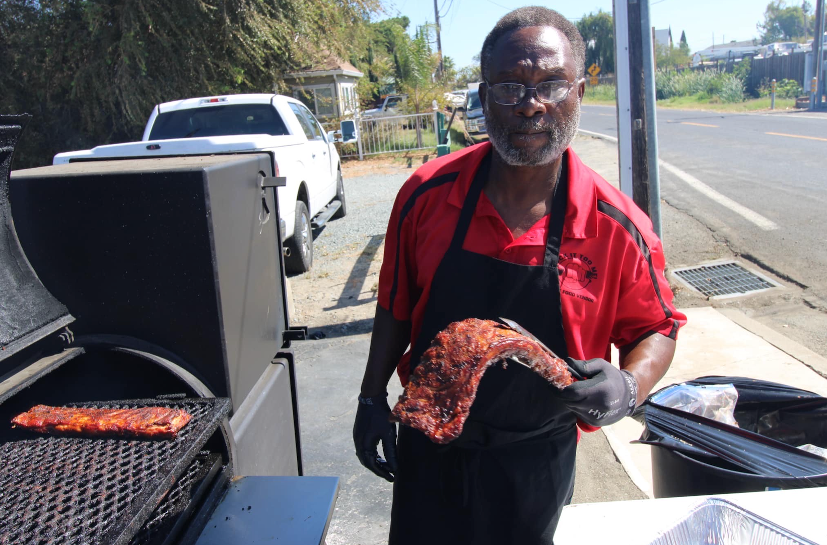 A man in an apron is holding a piece of meat in front of a grill