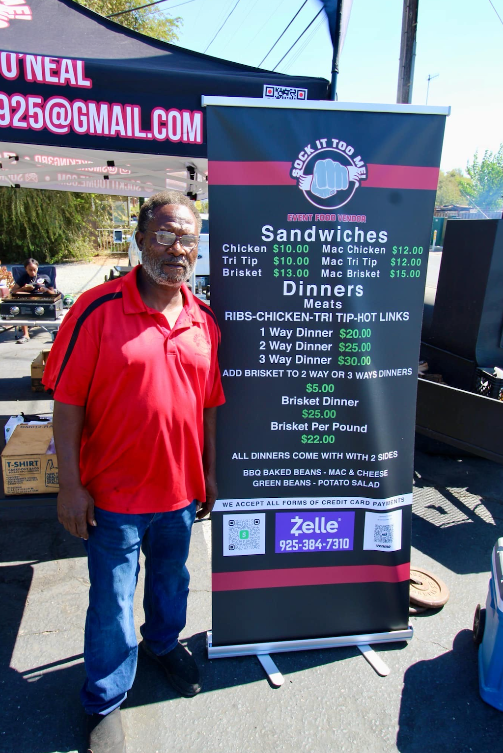 A man in a red shirt is standing in front of a sign for sandwiches and dinners