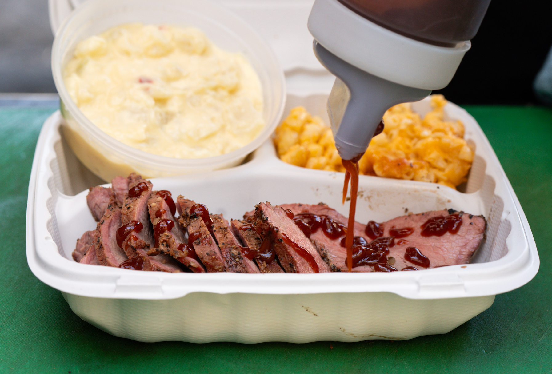 A person is pouring sauce on a tray of meat and macaroni and cheese.