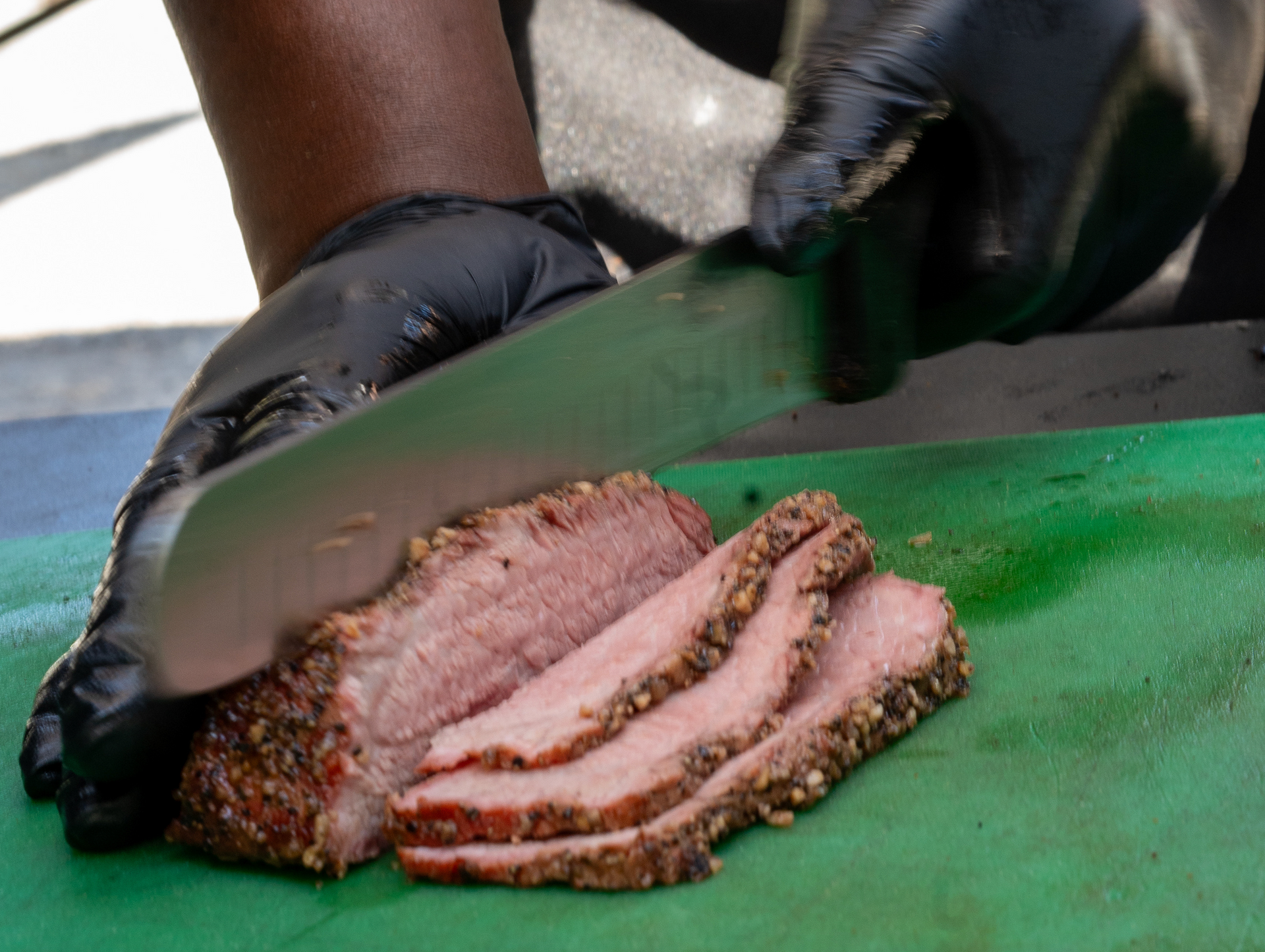 A person is cutting a piece of meat on a green cutting board.
