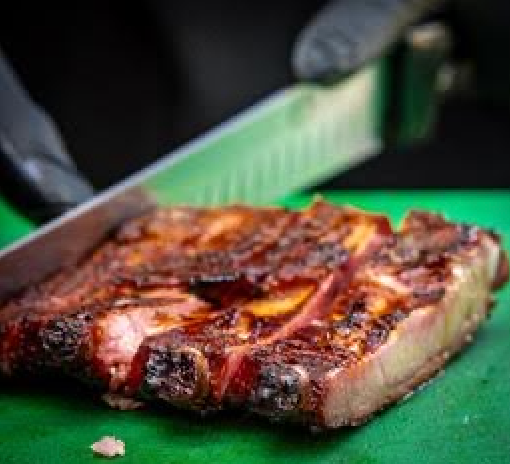 A person is cutting a piece of meat on a green cutting board.