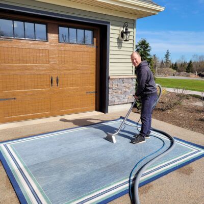 A man is vacuuming a rug in front of a garage door.