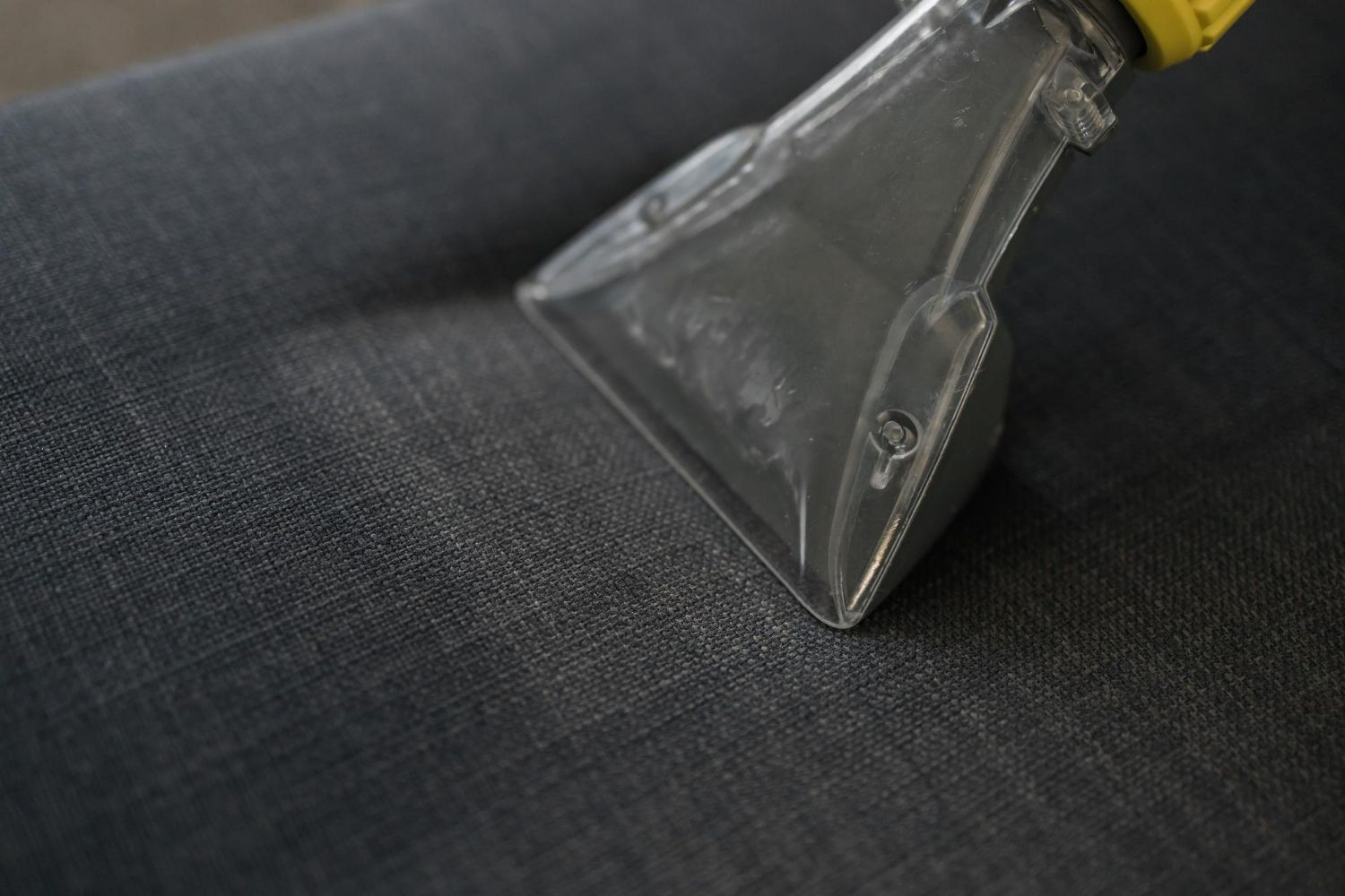 A close up of a vacuum cleaner cleaning a couch.