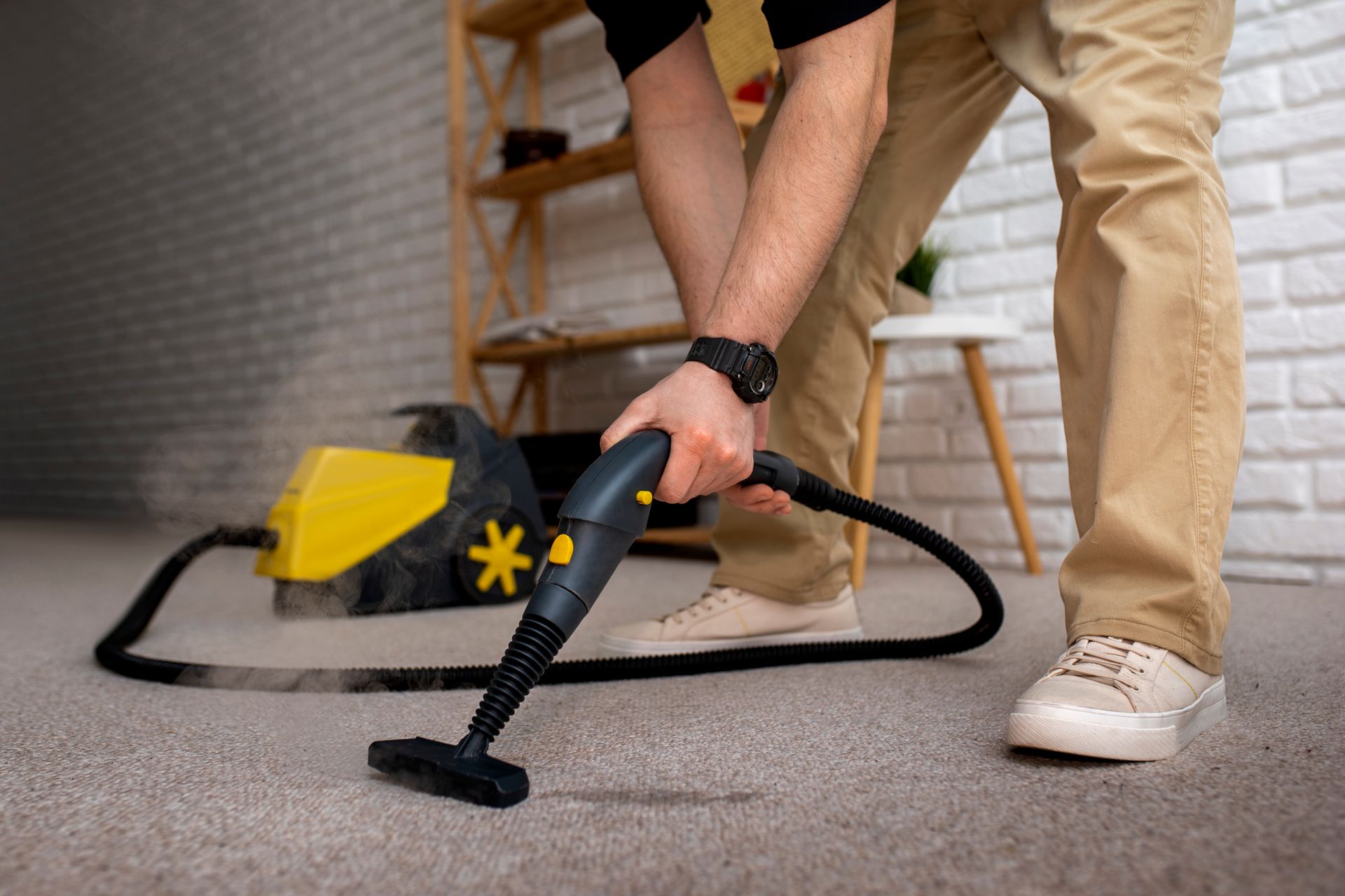 Person steam cleaning a carpet with a yellow and black machine in a room.