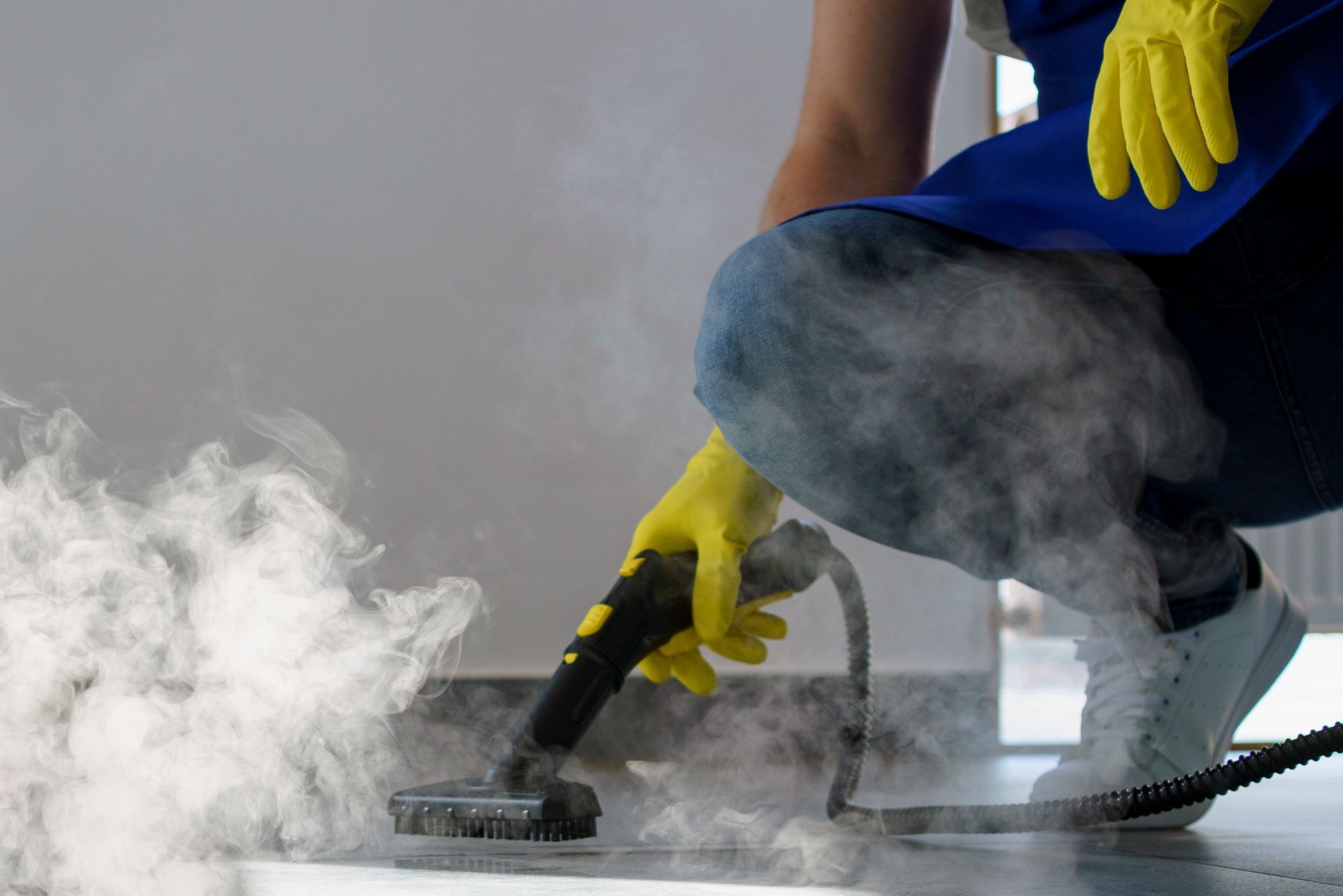 Person steam cleaning a floor with yellow gloves, creating a cloud of steam.