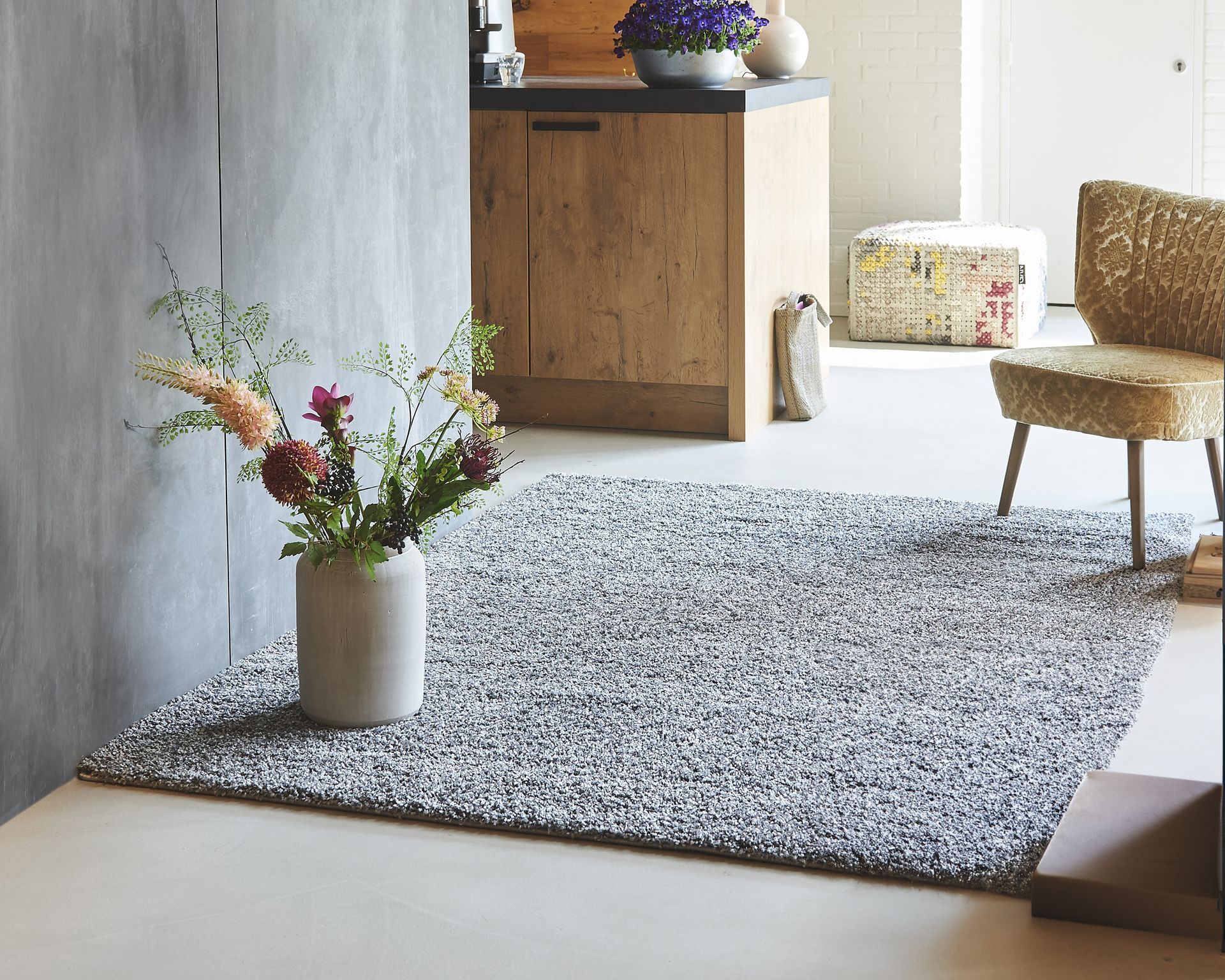 Shaggy gray rug on a light floor, vase of flowers, chair, and wooden cabinet in a room.