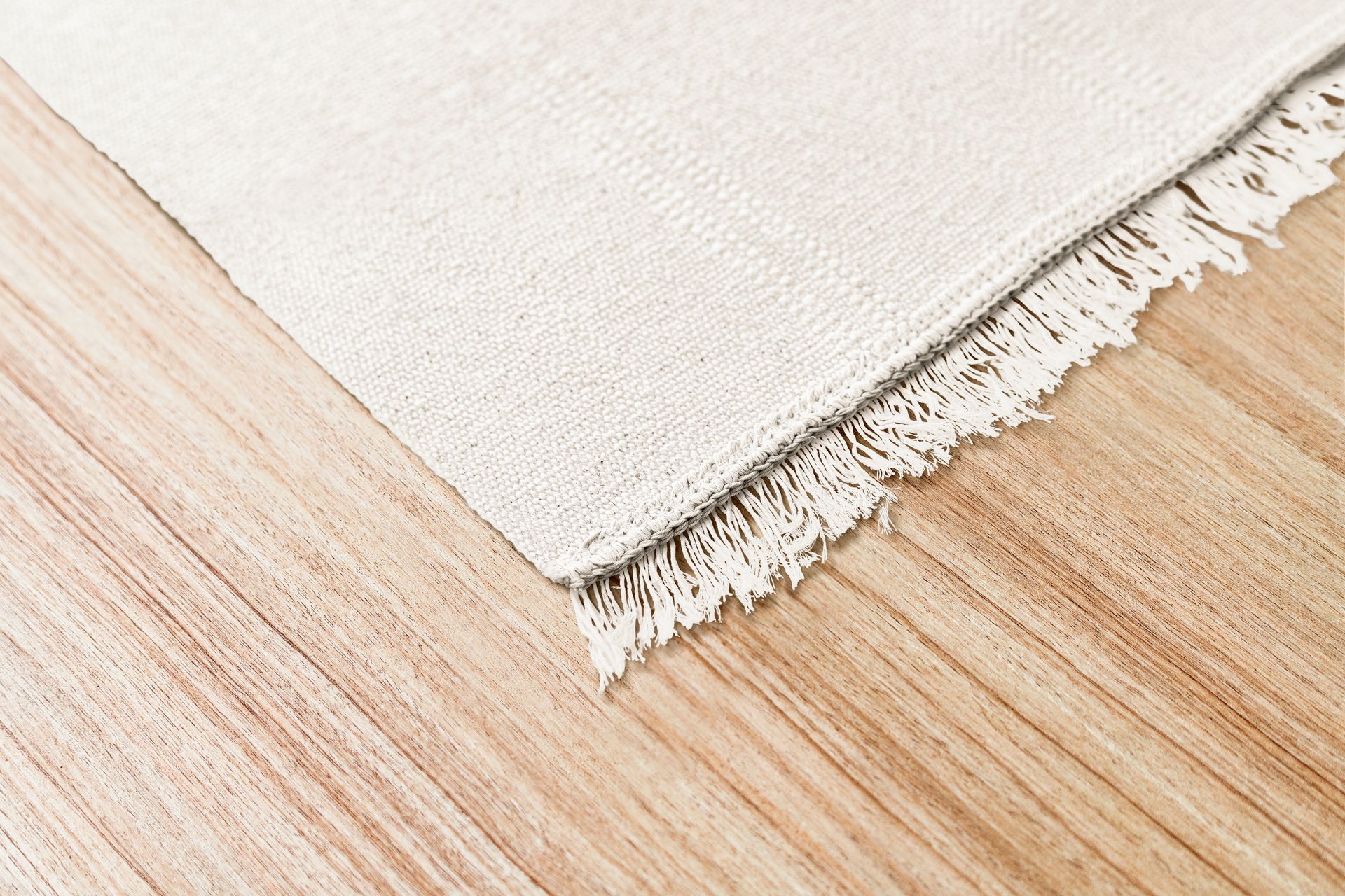 Beige woven rug with frayed edge on light wood floor.