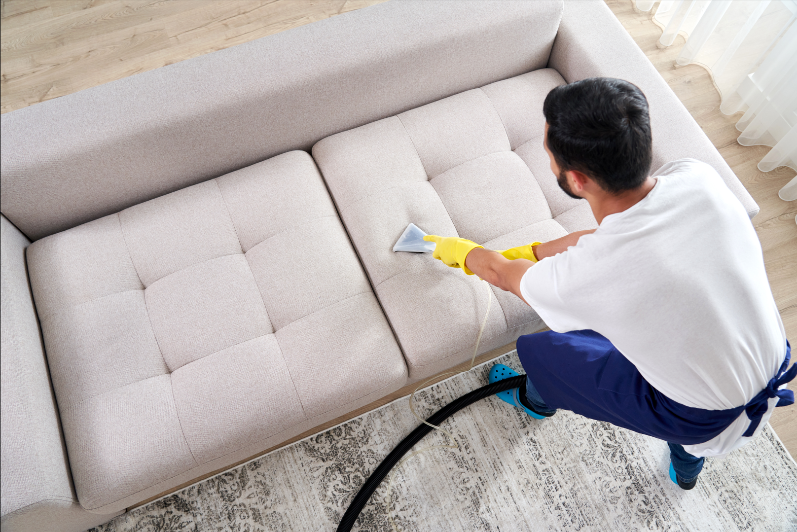 Worker using an upholstery extraction tool on a sofa.