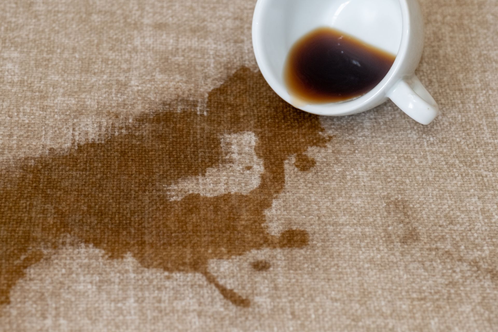 Spilled coffee from a cup on a fabric surface.
