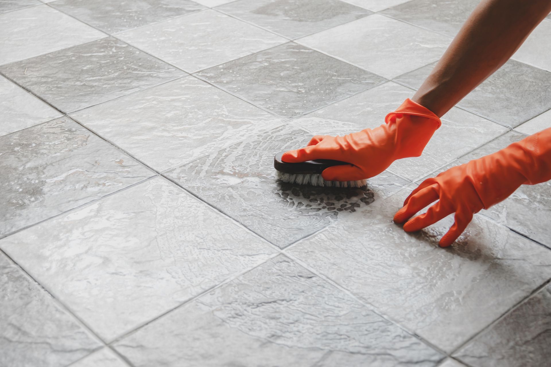 Hands in gloves scrubbing soapy tiled floor.