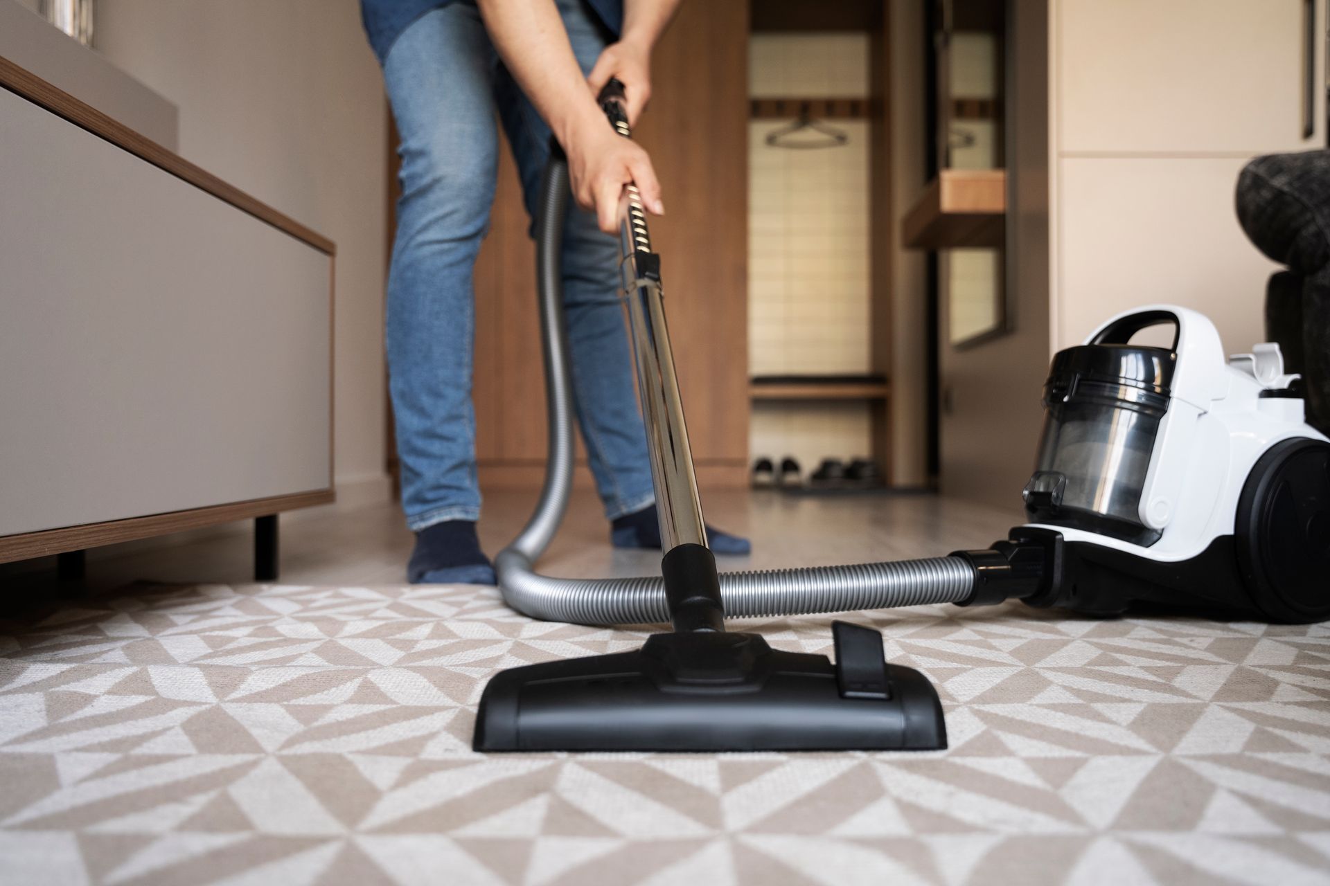 Person vacuuming a patterned rug with a canister vacuum.