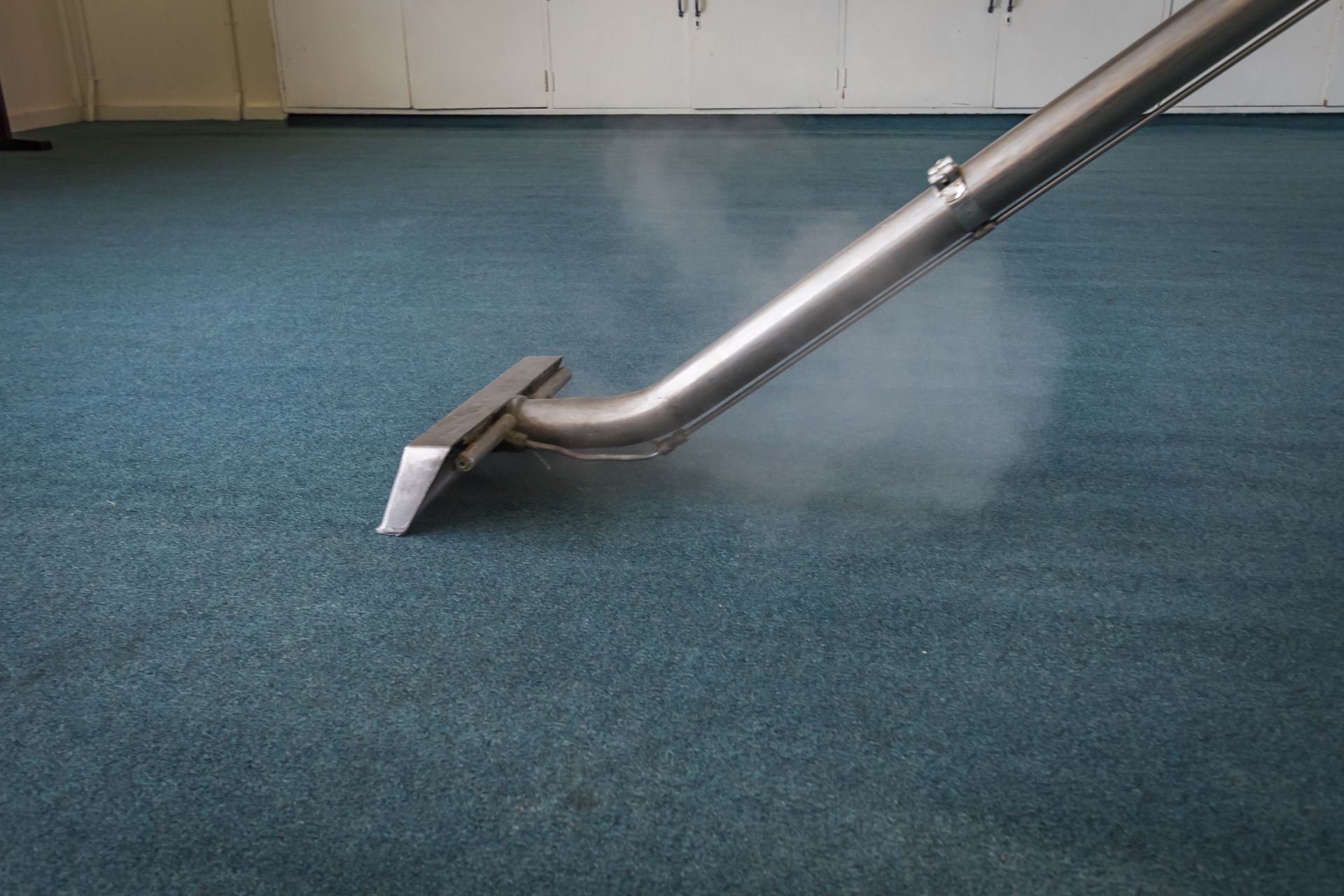 A vacuum cleaner is cleaning a blue carpet in a room.