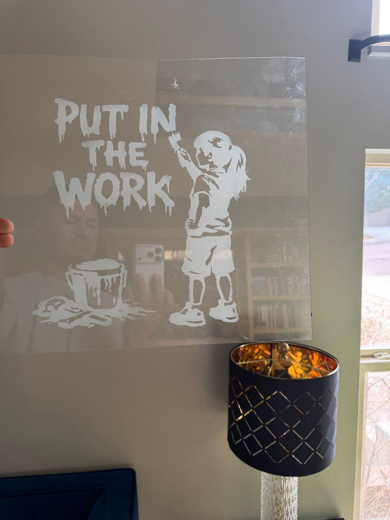 Wall decal reading “PUT IN THE WORK” above a black quilted lampshade in a gray room.