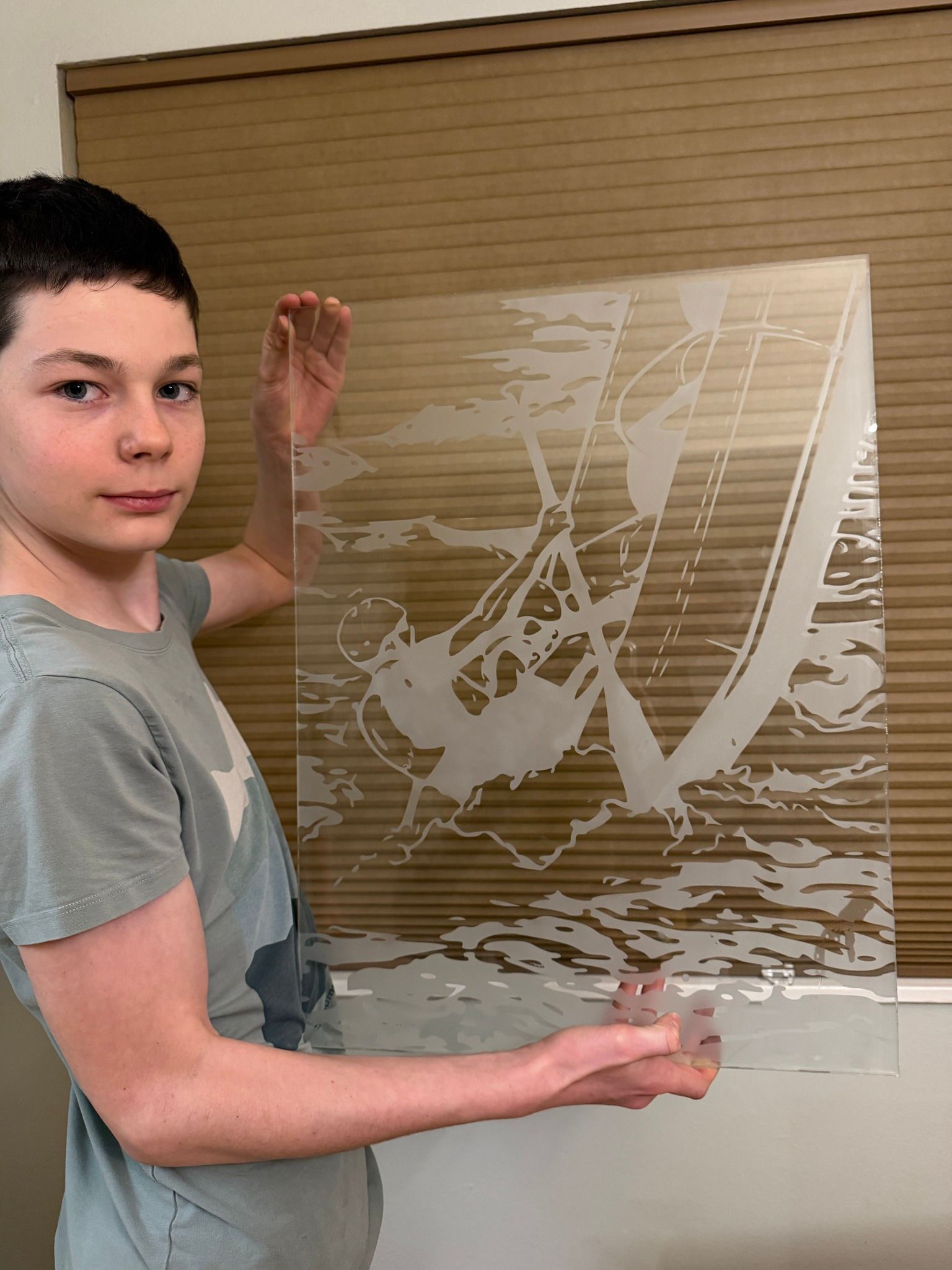 Person holding a clear etched glass panel indoors against a tan wall.