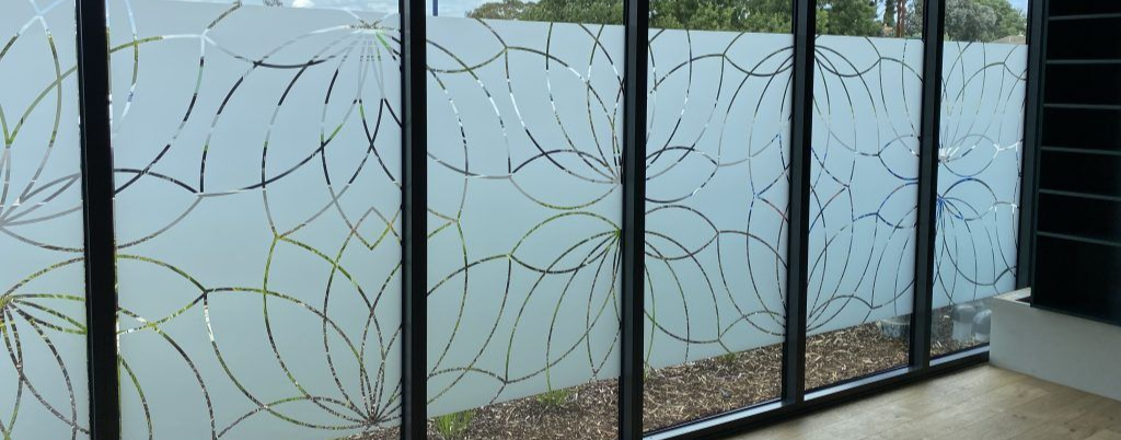 Frosted glass balcony railing with black frames and a gold leaf pattern, overlooking pebbles outside