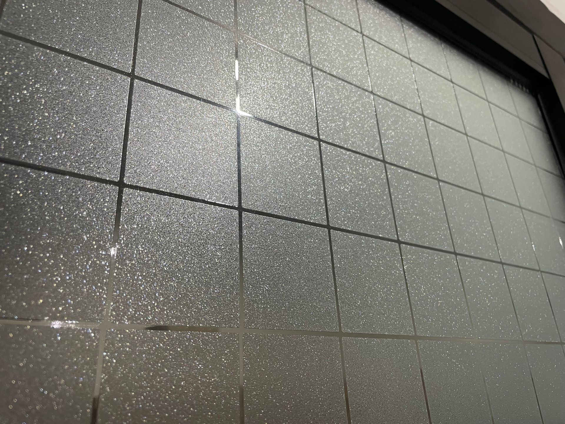 Gray tiled wall with a speckled surface and a dark frame along the top right.