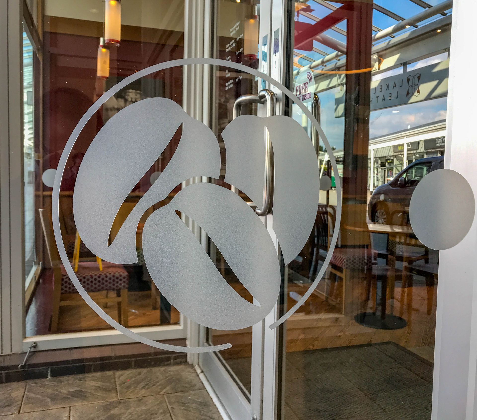 Glass storefront door with frosted leaf logo decals and a view into a cafe inside